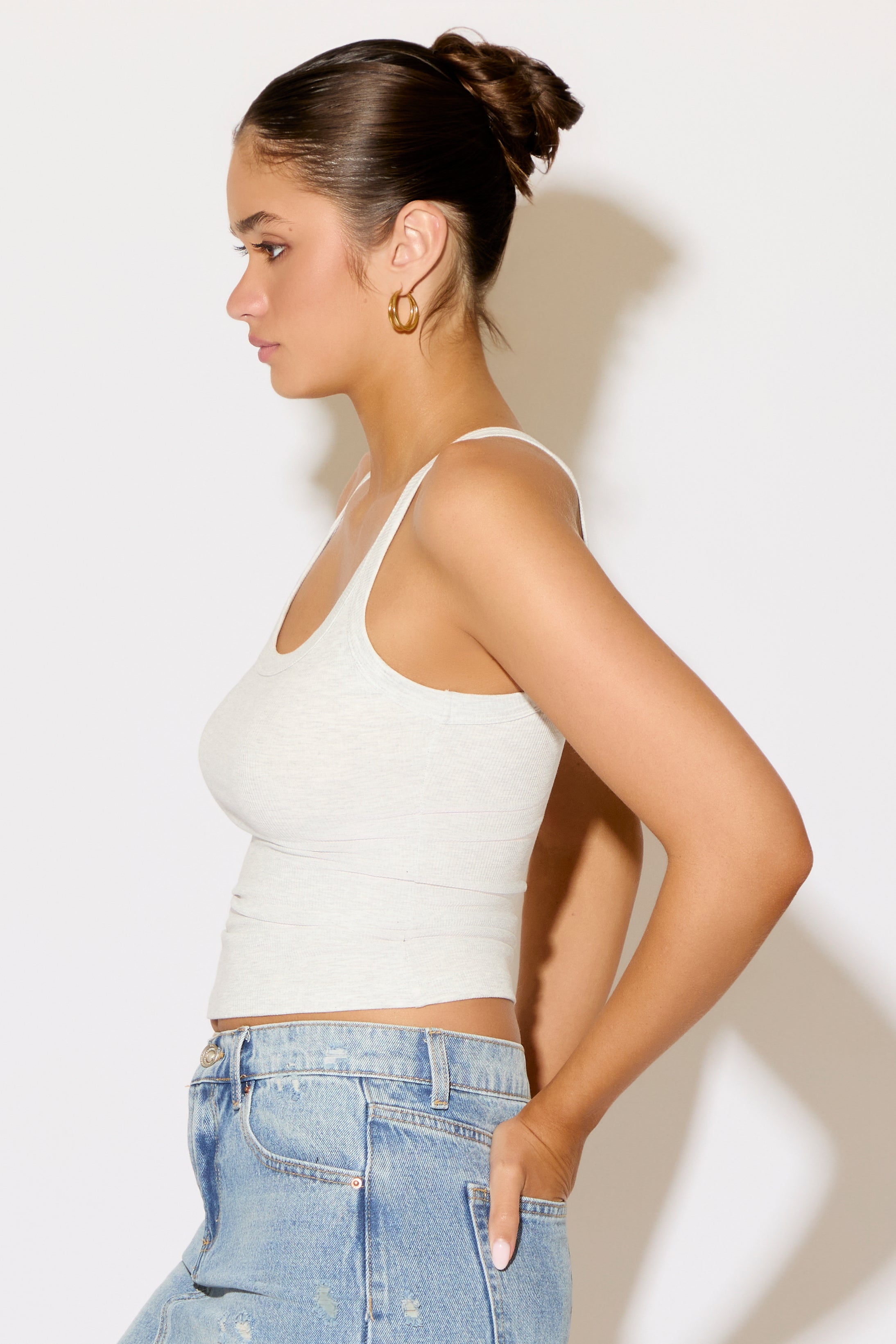 Woman wearing a white tank top and blue jeans against a plain background