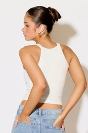 Woman wearing a white tank top and blue jeans against a plain background