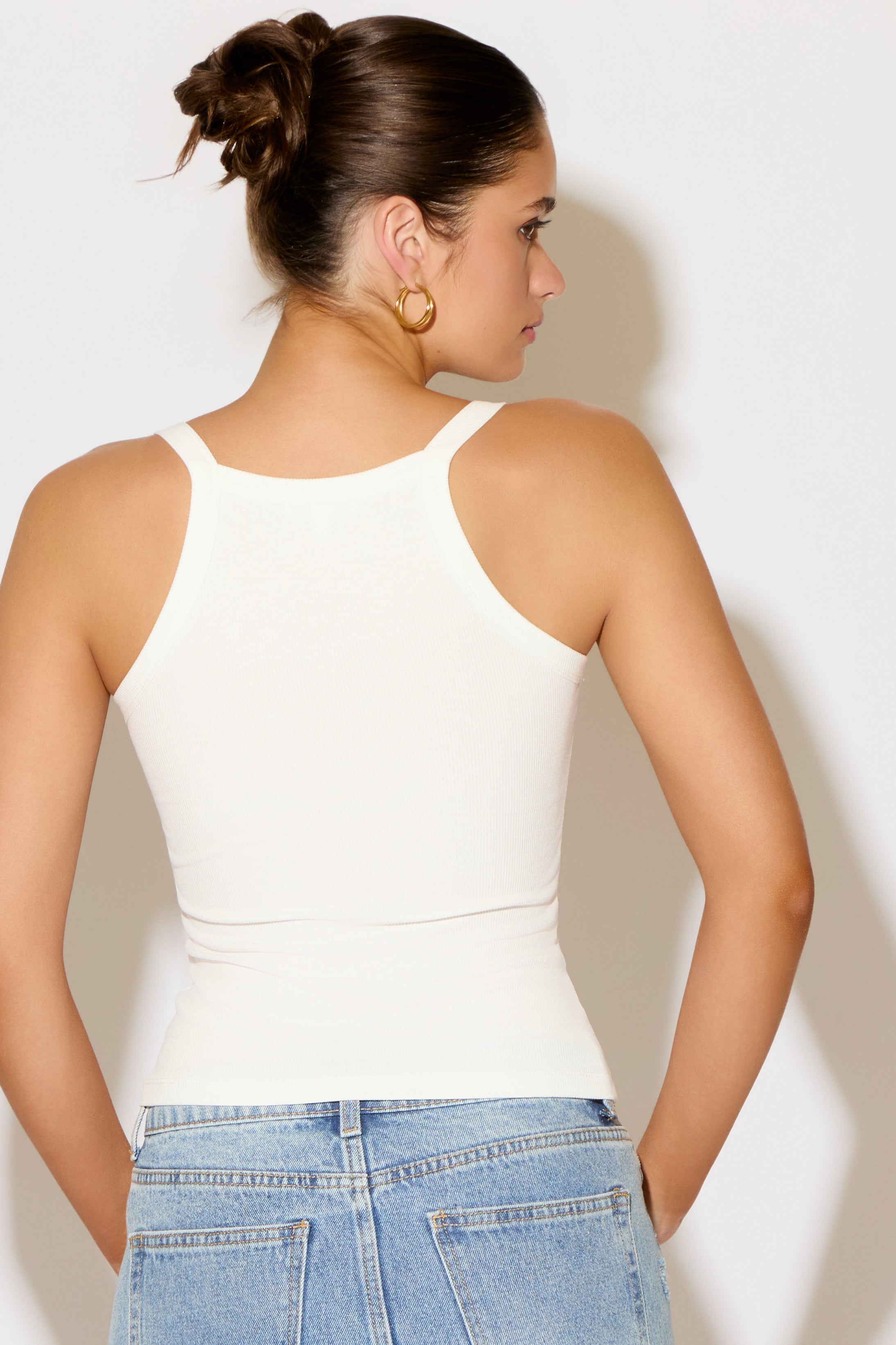 Woman wearing a white tank top and blue jeans against a plain background