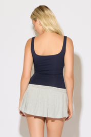 Model is wearing a navy scoop neck cropped rayon tank top with a heather grey skirt on a white background.