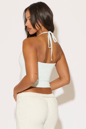 Woman wearing a white halter top with thin straps against a plain background