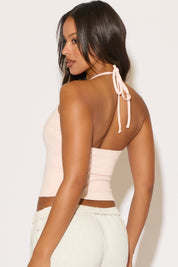 Woman wearing a light pink halter top with thin straps against a white background