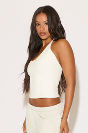 Woman wearing a white one-shoulder top and pants against a light background