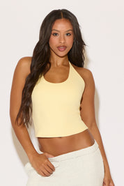 Woman wearing a yellow halter top and white pants against a light background