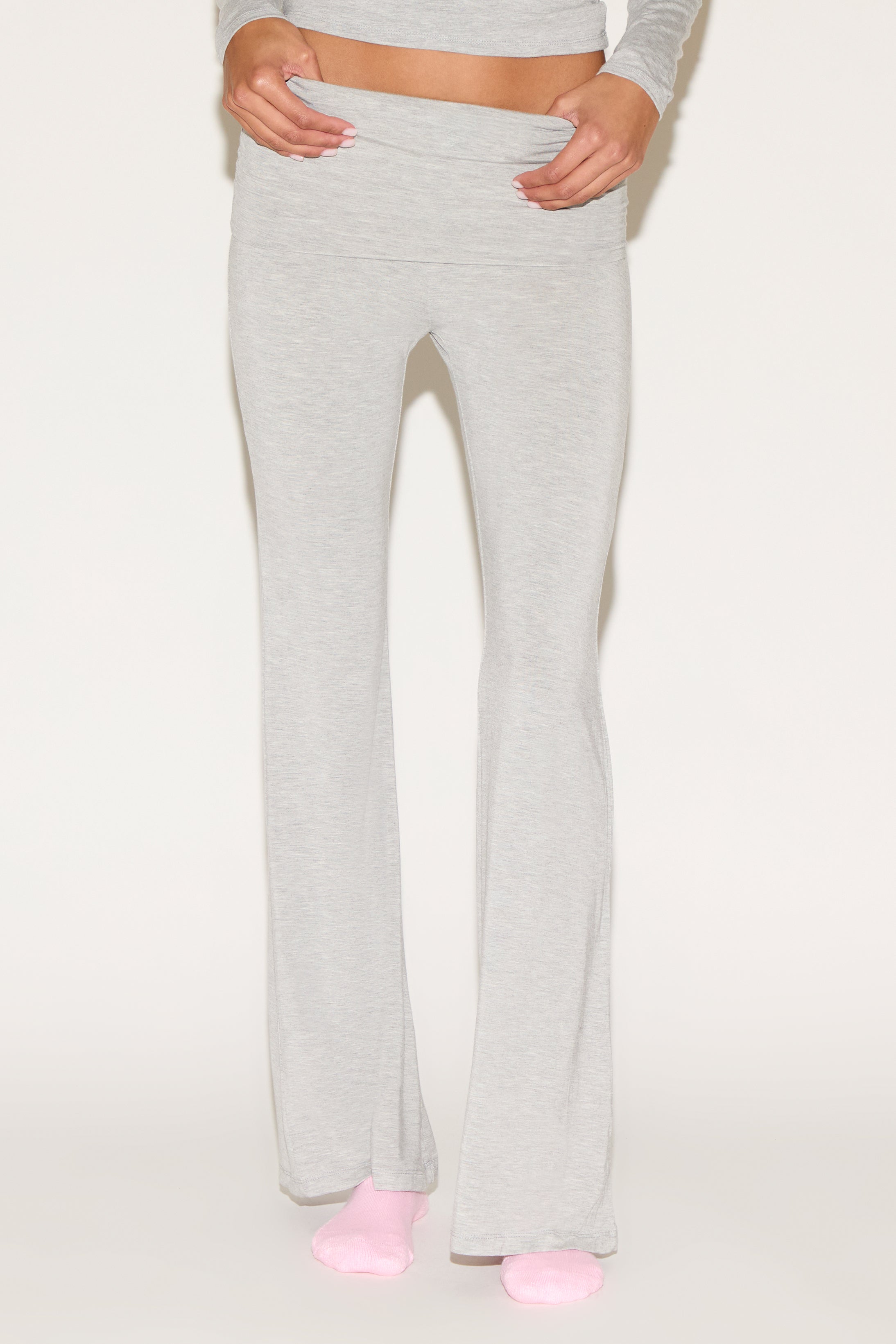 Model wearing grey low-rise flare pants with a fold-over waistband, styled with a grey long-sleeve top and pink socks against a neutral background.