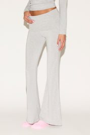 Model wearing grey low-rise flare pants with a fold-over waistband, styled with a grey long-sleeve top and pink socks against a neutral background.