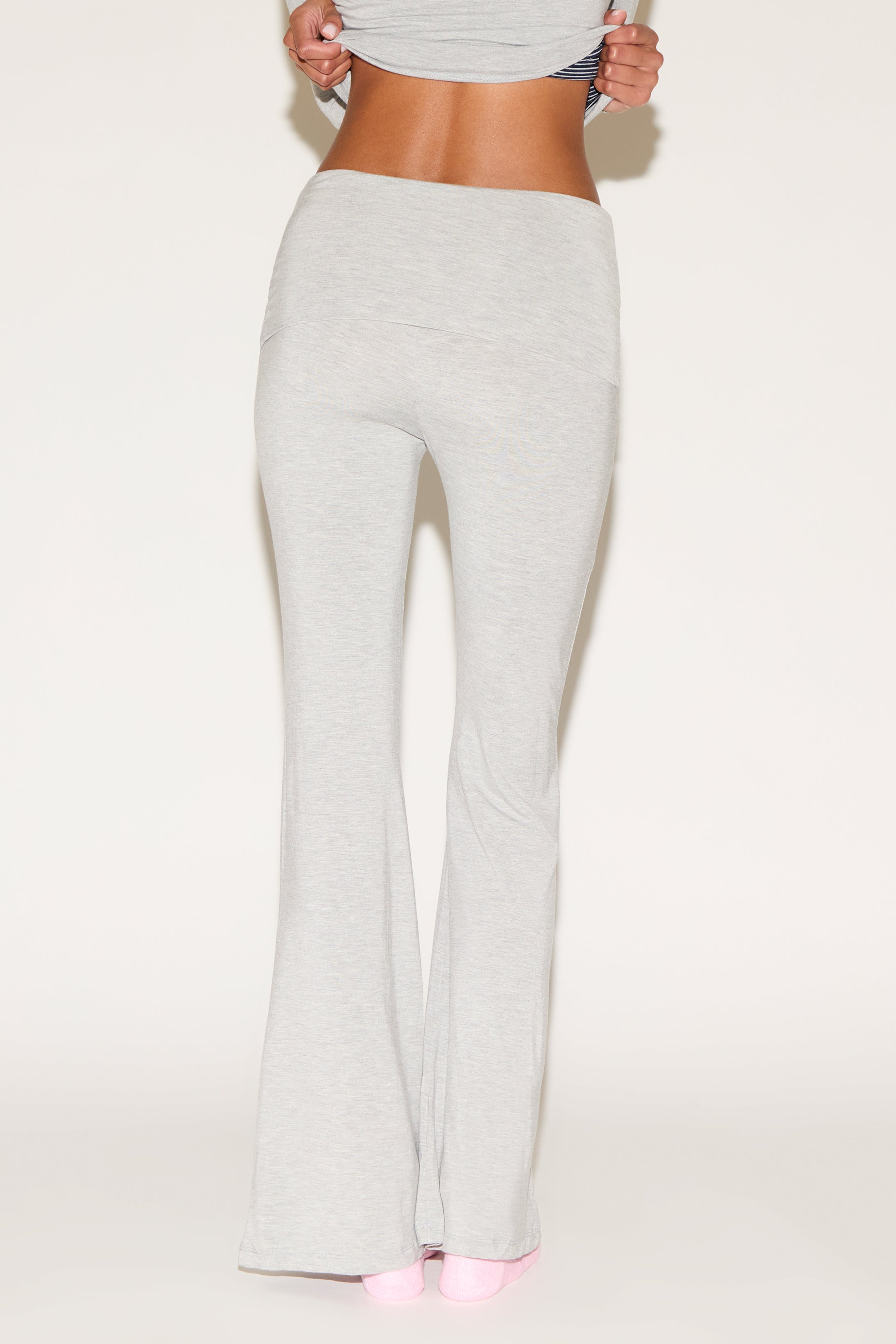 Model wearing grey low-rise flare pants with a fold-over waistband, styled with a grey long-sleeve top and pink socks against a neutral background.