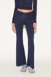 Model wearing navy low-rise flare pants with a fold-over waistband, styled with a navy long-sleeve top and light blue sneakers against a neutral background.