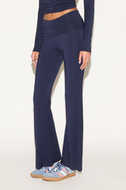 Model wearing navy low-rise flare pants with a fold-over waistband, styled with a navy long-sleeve top and light blue sneakers against a neutral background.