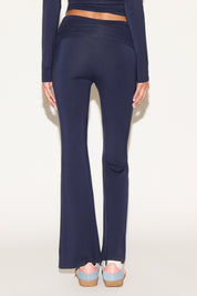 Model wearing navy low-rise flare pants with a fold-over waistband, styled with a navy long-sleeve top and light blue sneakers against a neutral background.