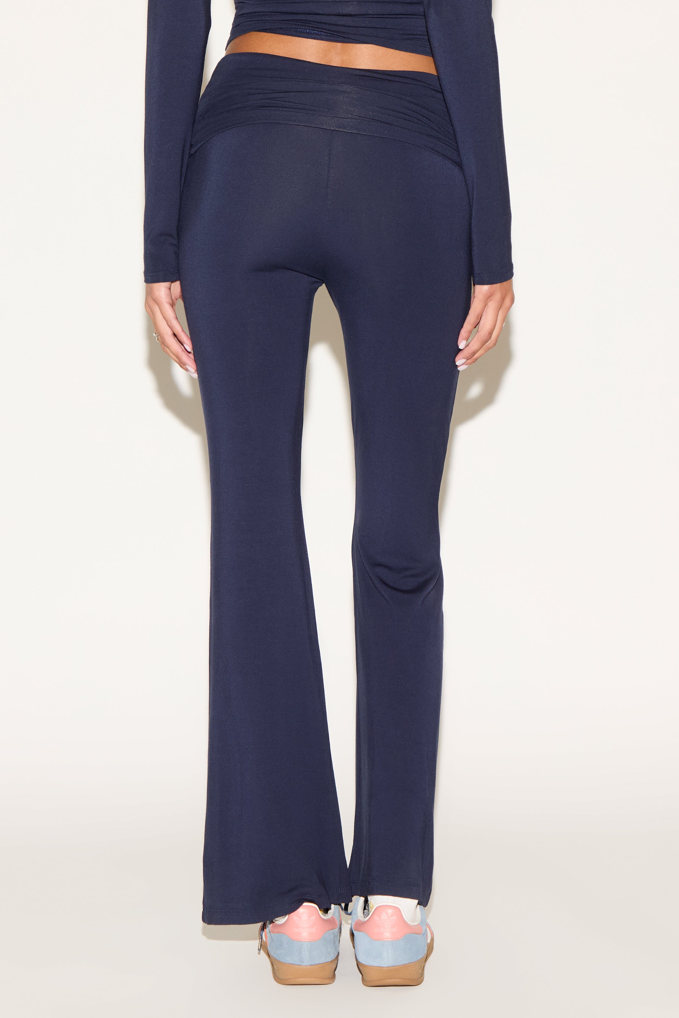 Model wearing navy low-rise flare pants with a fold-over waistband, styled with a navy long-sleeve top and light blue sneakers against a neutral background.