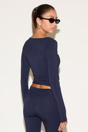 Back view of model wearing a navy long-sleeve fitted wrap top with matching bottoms, styled with black oval sunglasses and silver hoop earrings, hair in a sleek ponytail against a neutral background.
