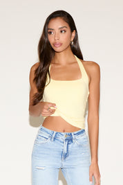 Woman wearing a yellow halter top and light blue jeans against a plain background