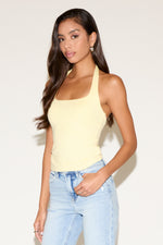Woman wearing a yellow tank top and light blue jeans against a plain background