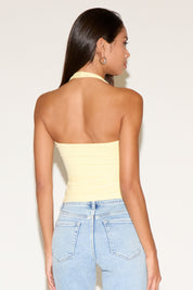 Woman wearing a yellow strapless top and light blue jeans against a plain background