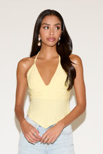 Woman wearing a yellow halter top and light blue jeans against a plain background