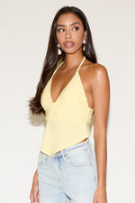 Woman wearing a yellow halter top and light blue jeans against a white background