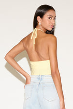Woman wearing a yellow halter top and light blue jeans against a white background