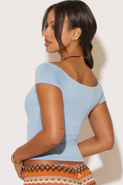 Woman wearing a light blue top and patterned skirt against a plain background