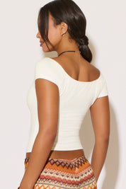 Woman wearing a white top and patterned skirt against a light background