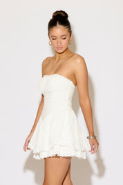 Woman wearing a white strapless dress against a plain background