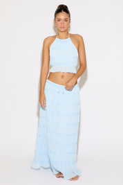 Woman wearing a light blue halter top and long skirt on a white background