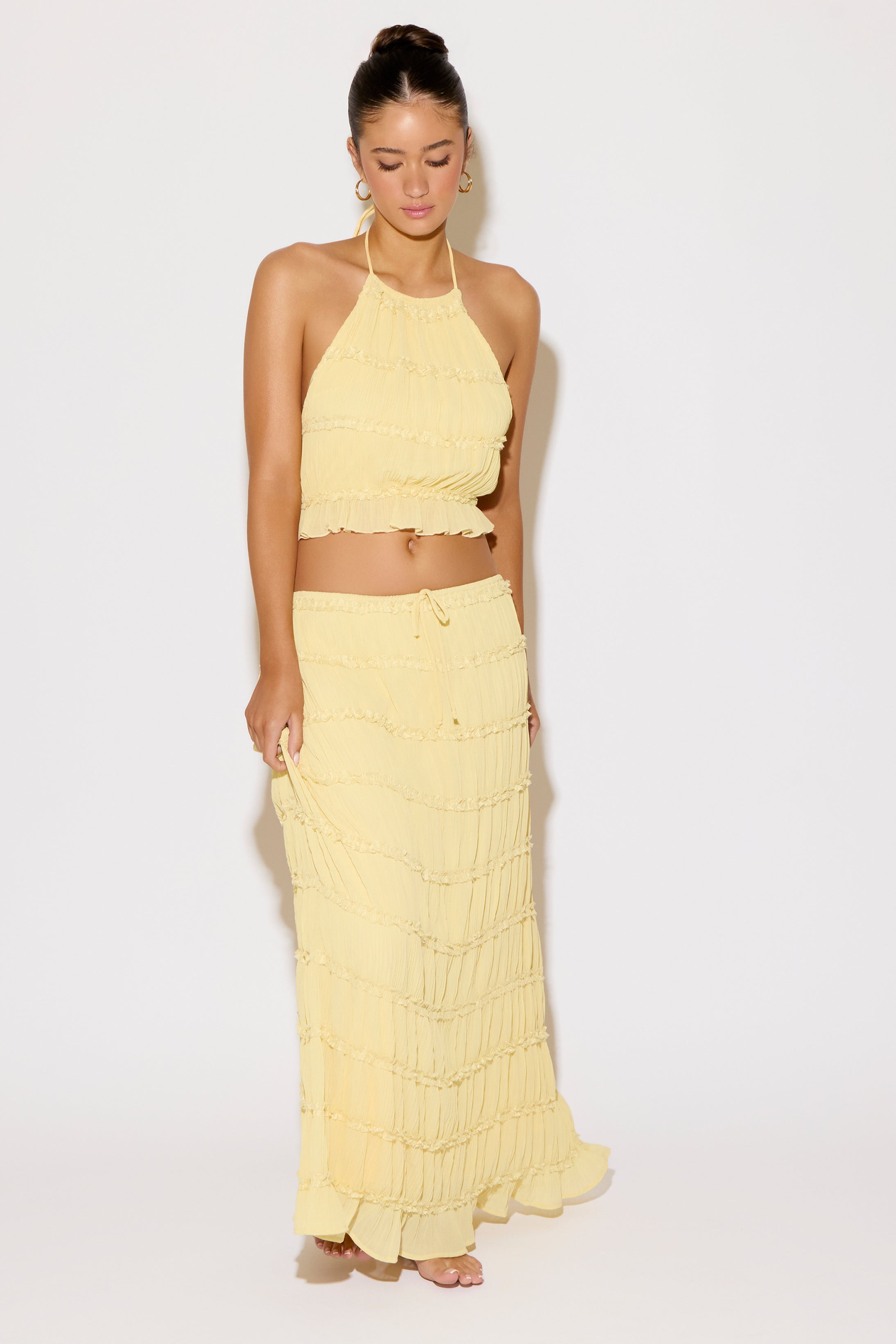 Woman wearing a yellow ruffled top and long skirt on a white background