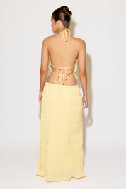 Woman wearing a yellow halter top and long skirt against a white background
