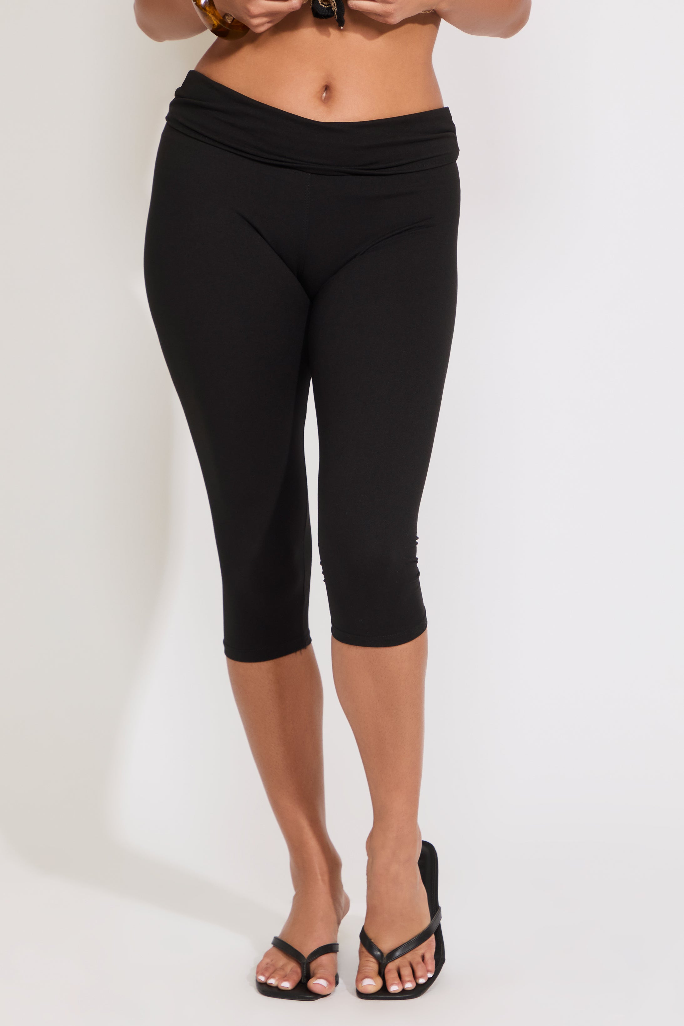 Model is wearing solid black capri legging with heels on a white background.