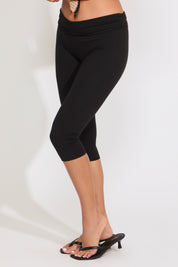 Model is wearing solid black capri legging with heels on a white background.