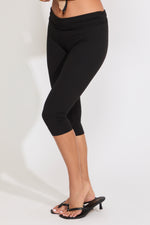 Model is wearing solid black capri legging with heels on a white background.