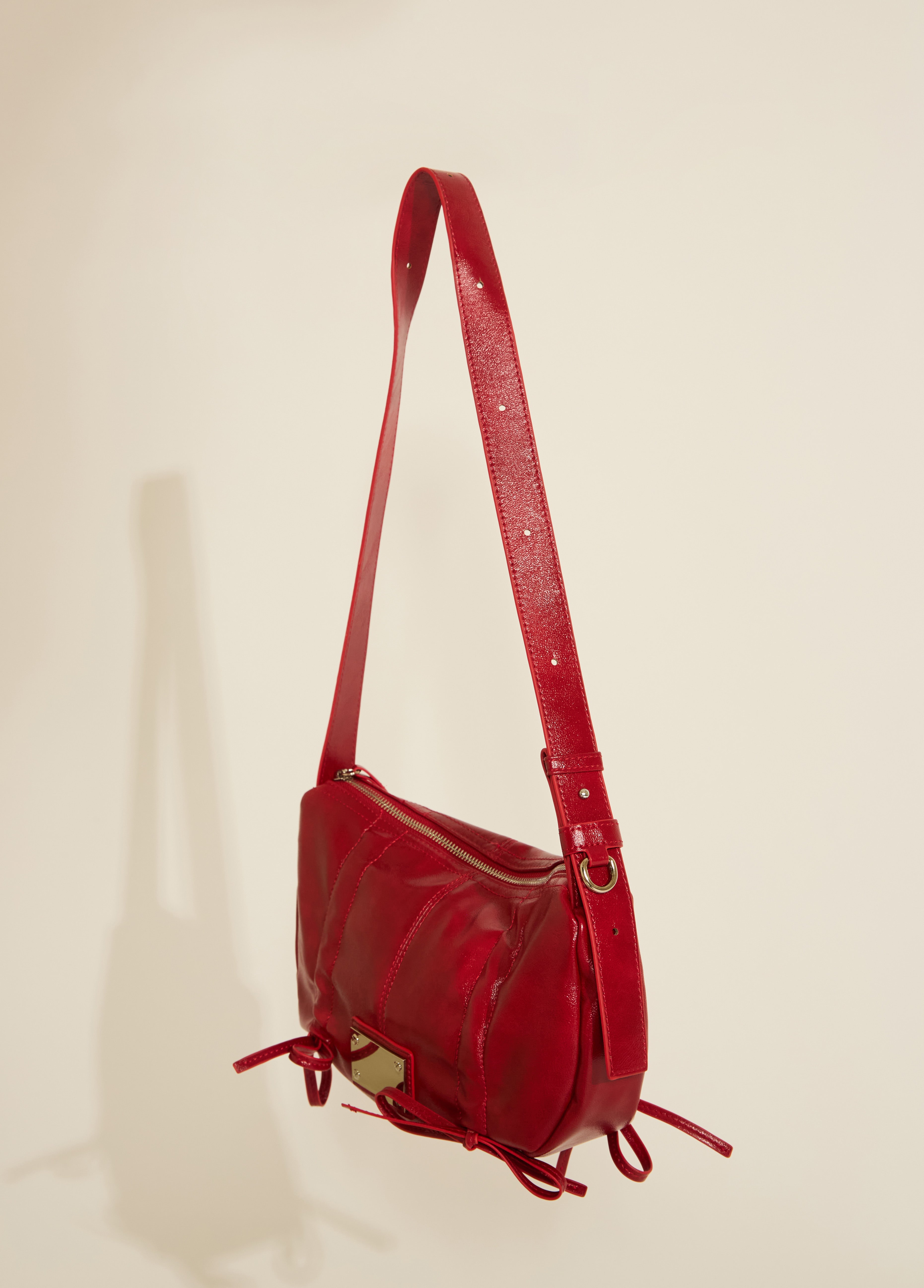 A red vegan leather handbag with scrunch tie details and silver hardware, displayed against a neutral background.