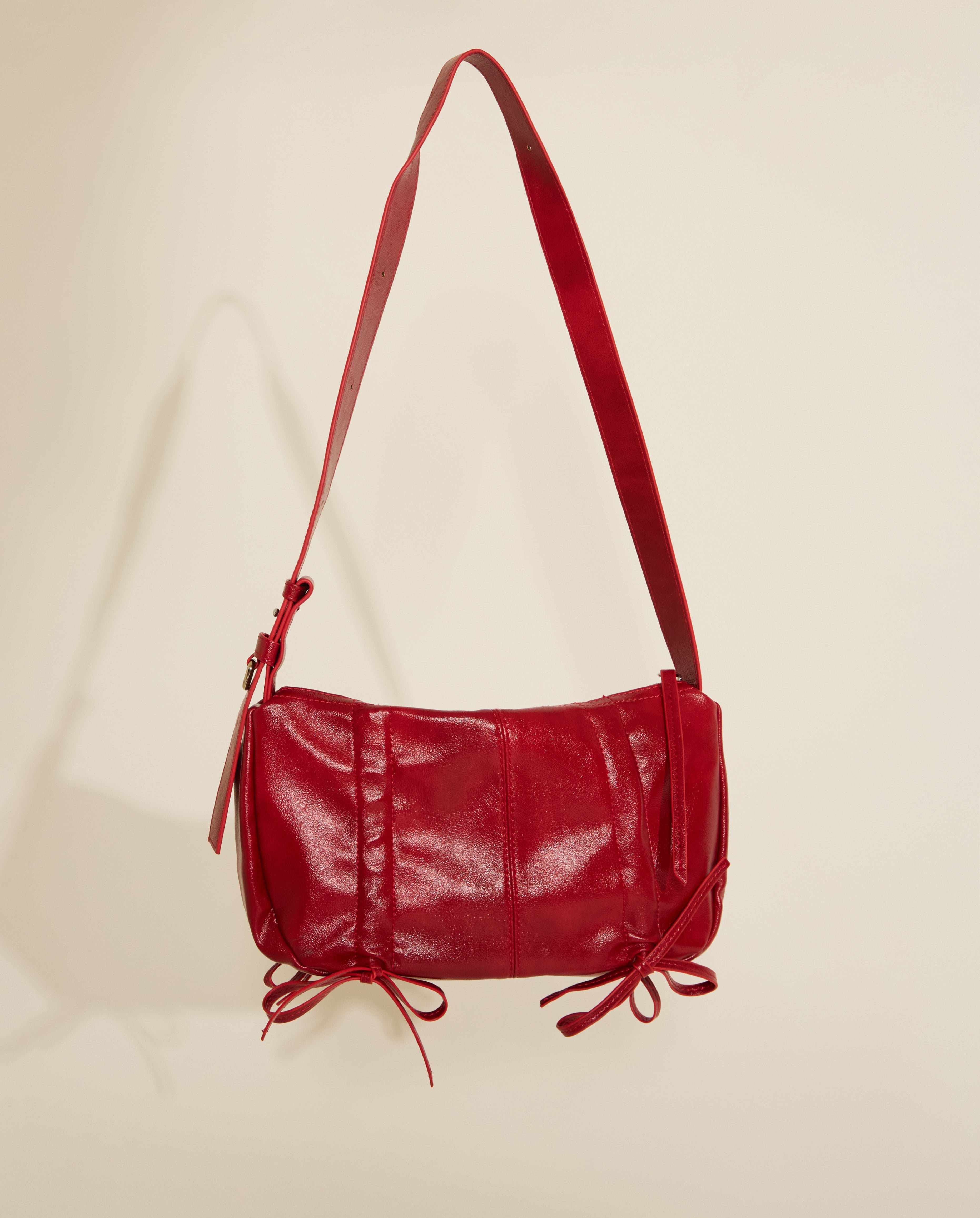 A red vegan leather handbag with scrunch tie details and silver hardware, displayed against a neutral background.
