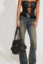 Model is wearing a hardware leather bag with jeans and crop top on a white background.