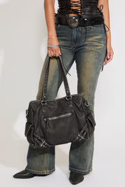 Model is wearing a hardware leather bag with jeans and crop top on a white background.
