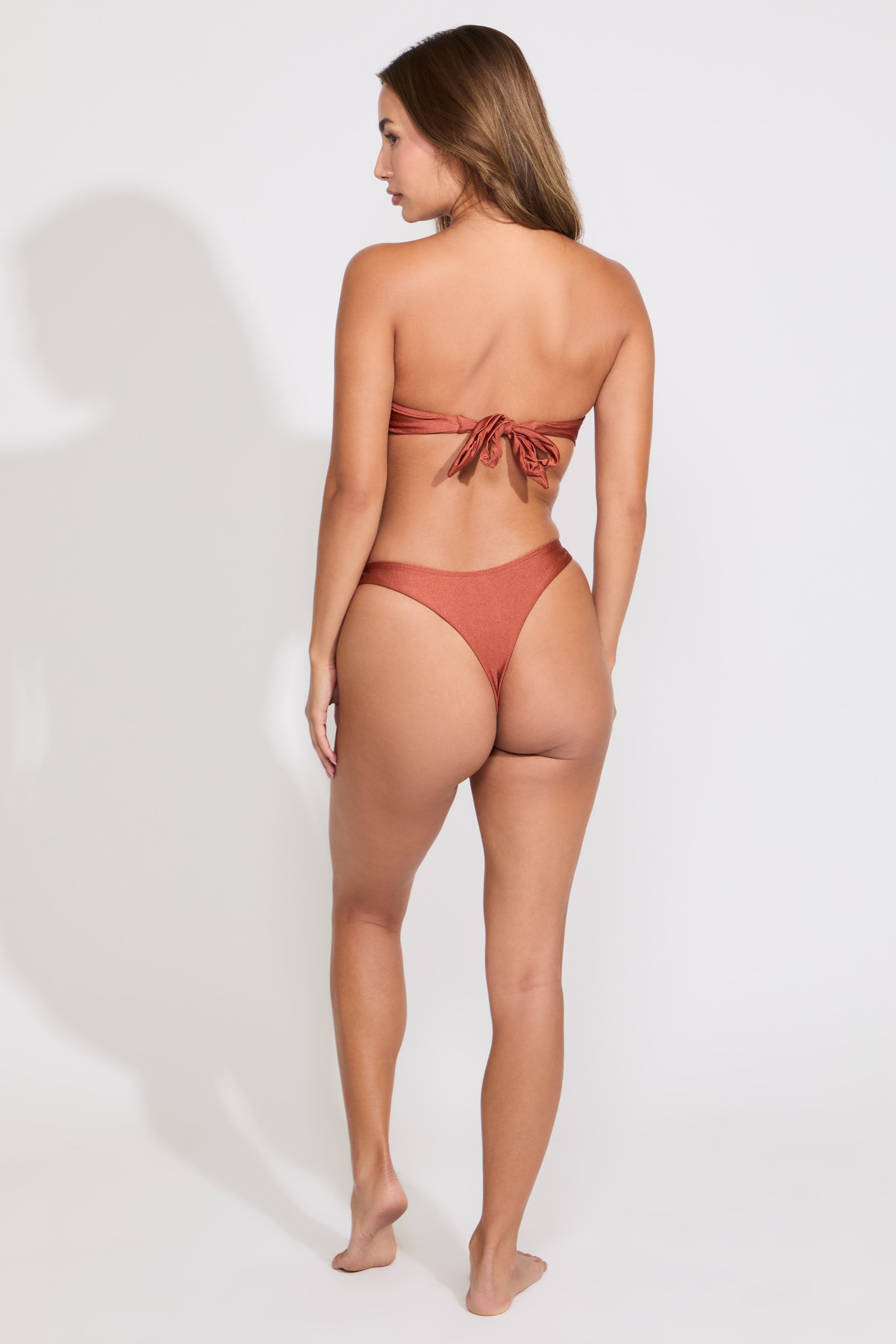 Model is wearing a brown strapless o ring top and hi cut bikini set on a white background.