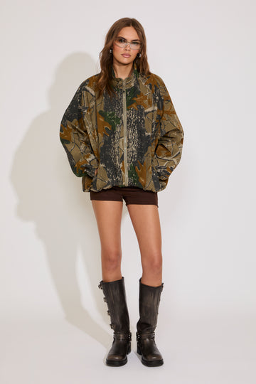 Person wearing a camouflage jacket and black boots on a white background
