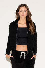 Woman wearing a black jacket, black top, and black pants with white drawstring on a white background