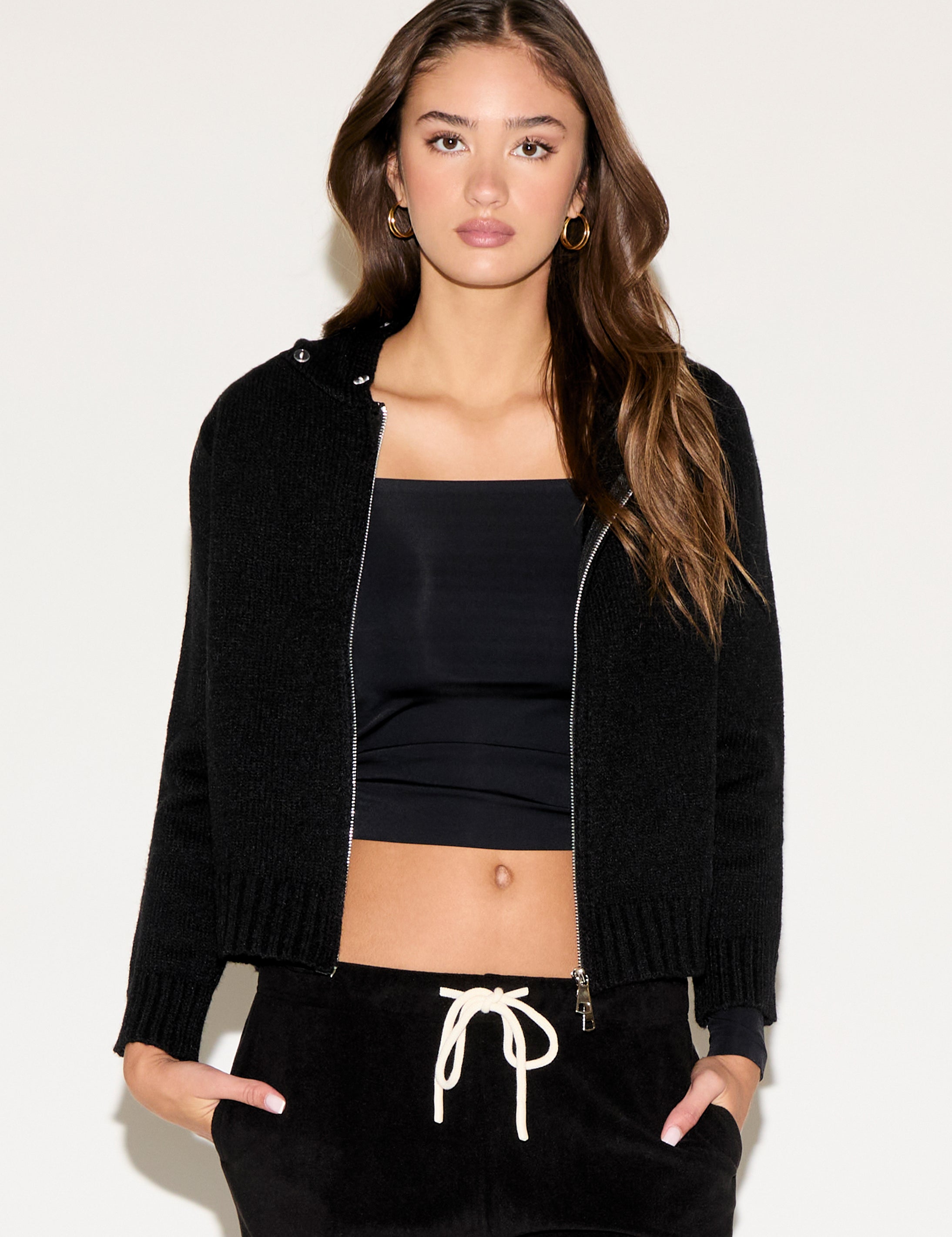 Woman wearing a black jacket, black top, and black pants with white drawstring on a white background