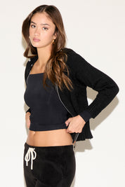 Woman wearing a black cropped top and cardigan with black pants on a white background