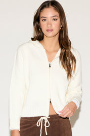 Woman wearing a white zip-up hoodie against a plain background