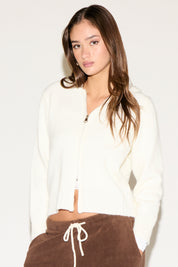 Woman wearing a white cardigan over a brown outfit on a plain background