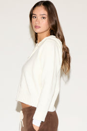Woman wearing a white sweater over a brown outfit on a plain background