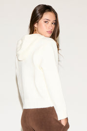 Woman wearing a white sweater and brown pants on a plain background