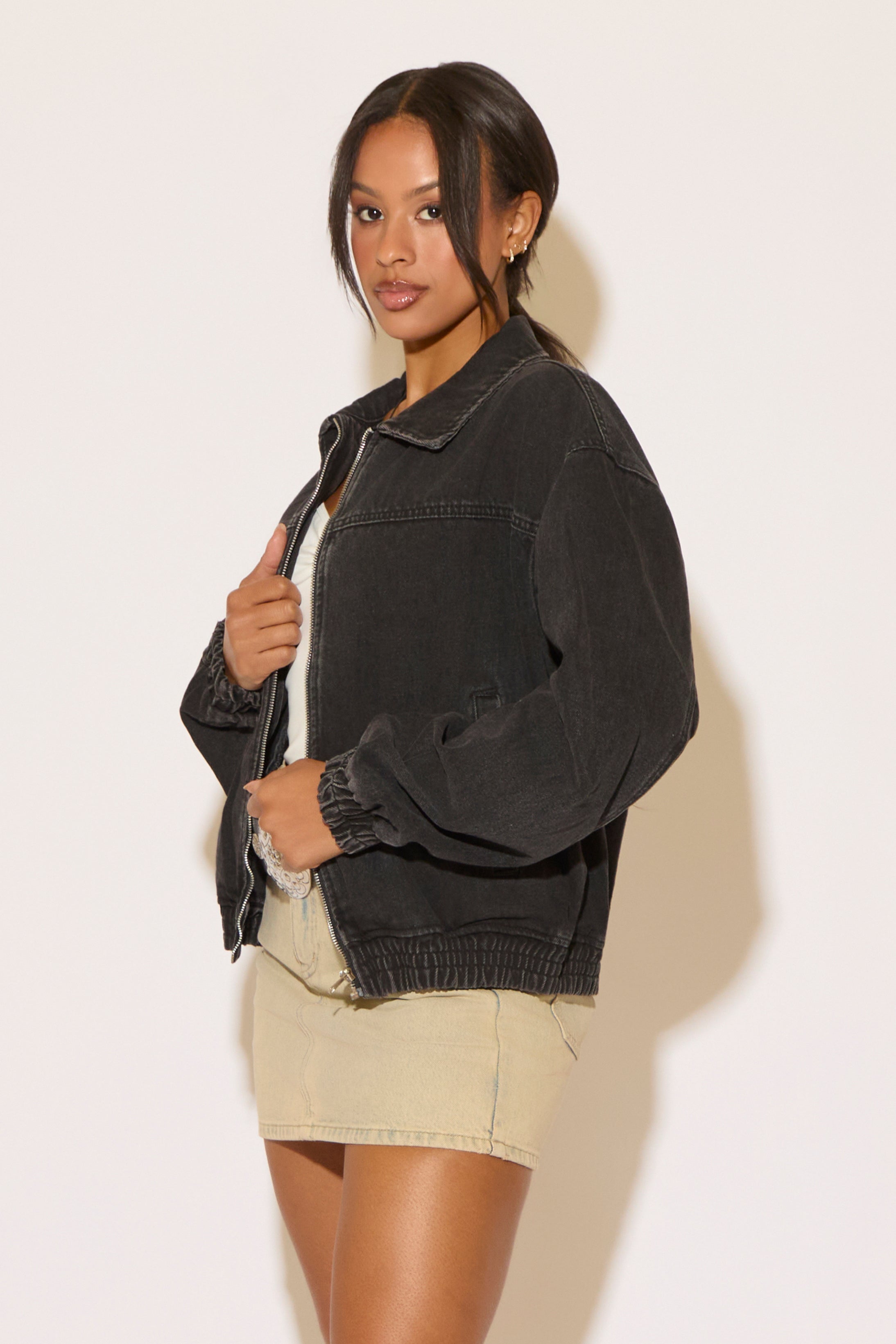 Woman wearing a black denim jacket, white top and khaki skirt on a white background