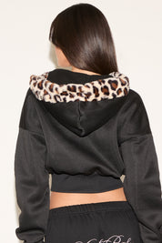 Black hoodie with leopard print trim worn by a person on a plain background