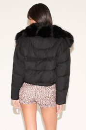 Person wearing a black puffer jacket with fur hood on a plain background