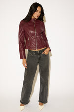 Woman wearing a burgundy leather jacket and gray jeans on a white background