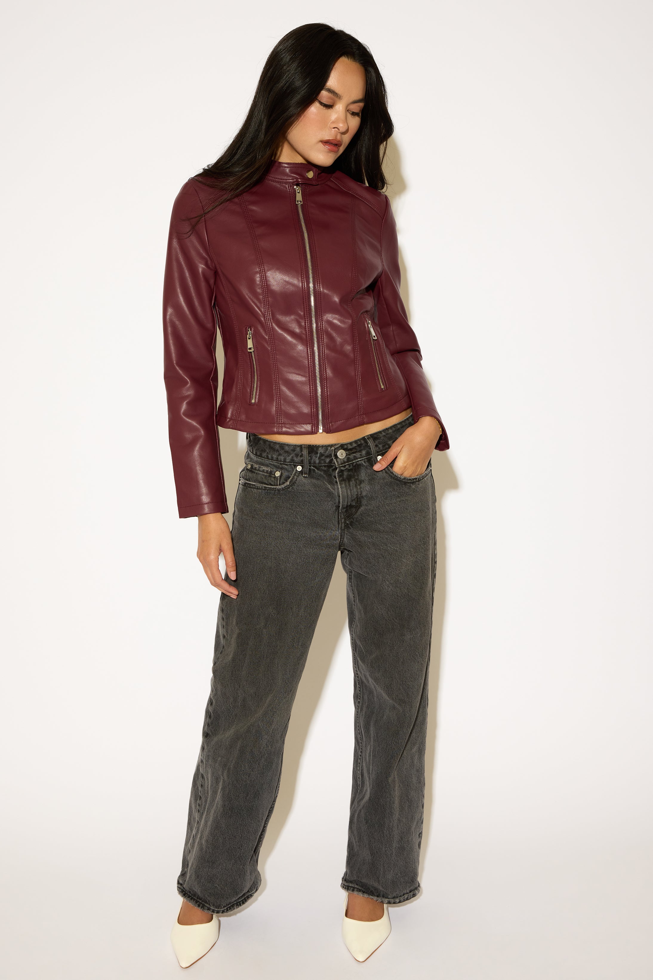 Woman wearing a burgundy leather jacket and gray jeans on a white background