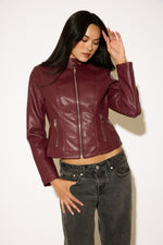Woman wearing a burgundy leather jacket and gray jeans against a white background